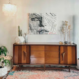 Wooden sideboard in a living room with abstract art, plants, and a rug.