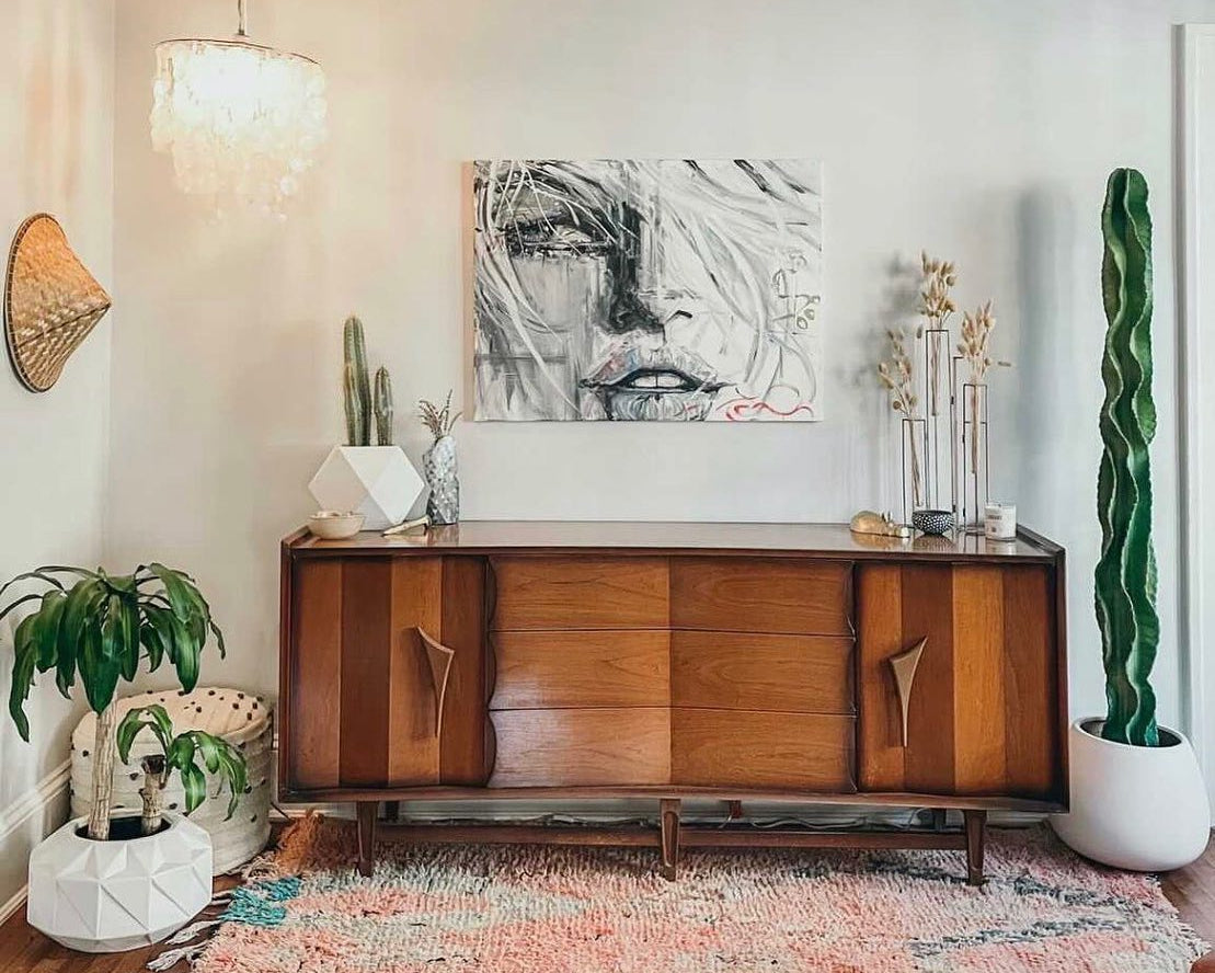 Wooden sideboard in a living room with abstract art, plants, and a rug.